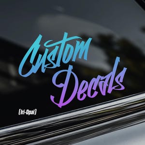 May include: A custom decal with the words "Custom Decals" in a gradient of blue and purple. The decal is displayed on a car window. The text "[Iri-Opal]" is below the words. A logo is in the upper left corner.
