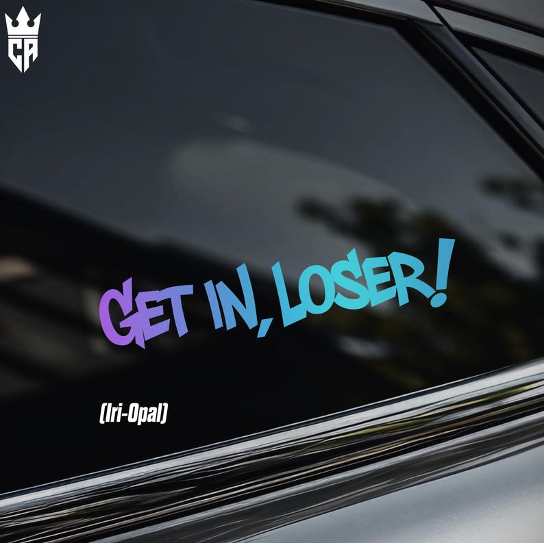 May include: A vinyl decal applied to a car window featuring the text "GET IN, LOSER!" in a stylized, bold font. The lettering displays a gradient color transition from purple on the left to a bright cyan blue on the right side.