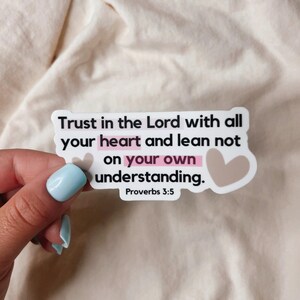 May include: White sticker with the text "Trust in the Lord with all your heart and lean not on your own understanding. Proverbs 3:5" in black text with a pink heart around the word "heart" and a brown heart to the right of the text.