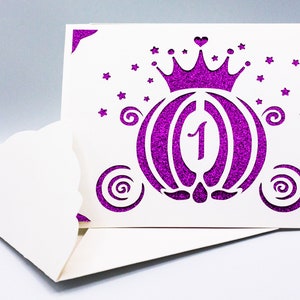 May include: A white card with a purple glitter design of a carriage with a crown on top. The number "1" is inside the carriage. The card has a scalloped edge.