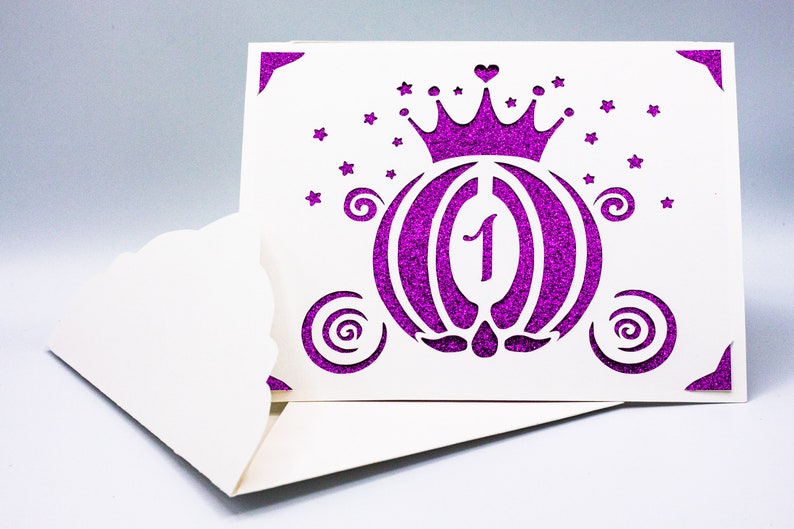 May include: A white card with a purple glitter design of a carriage with a crown on top. The number "1" is inside the carriage. The card has a scalloped edge.