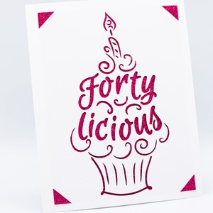 May include: A white card with a pink glitter design of a cupcake with a candle and the text "Forty Licious".