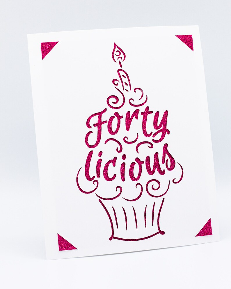 May include: A white card with a pink glitter design of a cupcake with a candle and the text "Forty Licious".