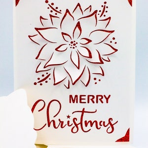 May include: A white card with a red glitter design of a poinsettia flower and the text "Merry Christmas".