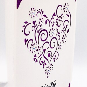 May include: A white card with a purple heart-shaped design featuring intricate swirls and flowers. The text "Nicole & Rhys" and "April 20, 2022" is printed in black at the bottom of the card.