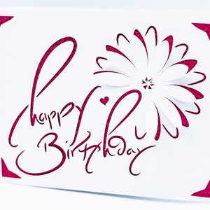 May include: A white card with pink glitter lettering that says "Happy Birthday" with a pink and white paper flower in the corner.
