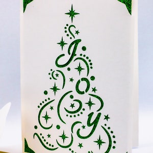 May include: A white card with a green glitter design of a Christmas tree with the word "Joy" inside. The tree is decorated with stars and swirls.