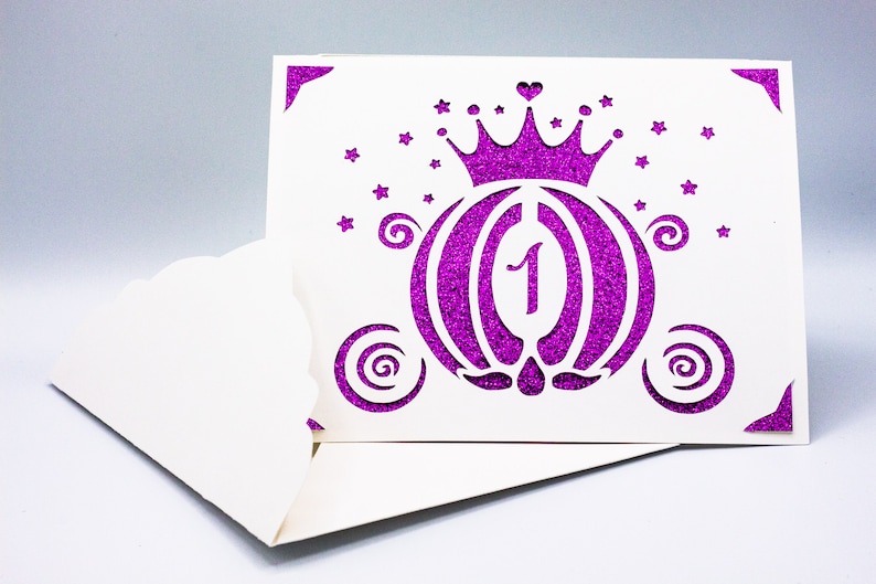 May include: A white card with a purple glitter design of a carriage with a crown on top. The number "1" is in the center of the carriage. The card has a scalloped edge.