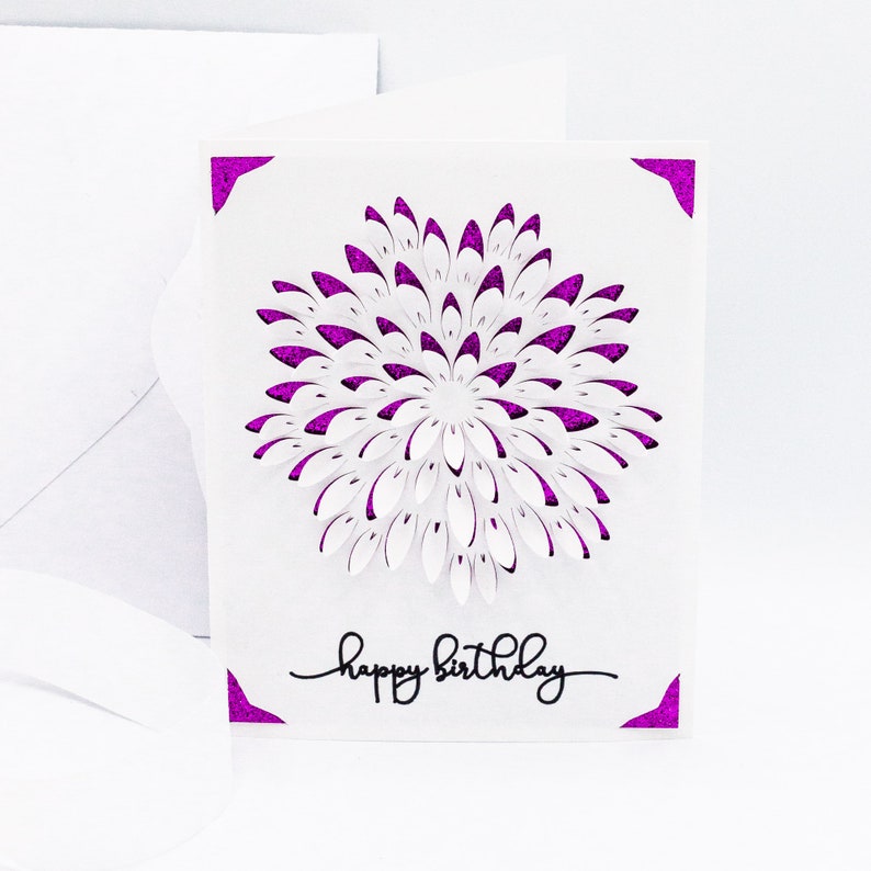 May include: A white card with a purple glitter border and a white paper cut-out flower design. The card says "happy birthday" in black script.