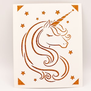 Puede incluir: Una tarjeta blanca con una silueta de unicornio dorada con purpurina y estrellas. El unicornio tiene un ojo cerrado y un cuerno rizado.