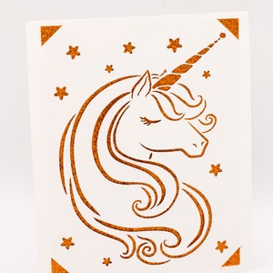 Puede incluir: Una tarjeta blanca con una silueta de unicornio marr&oacute;n con purpurina y estrellas. El unicornio tiene un ojo cerrado y un cuerno rizado.
