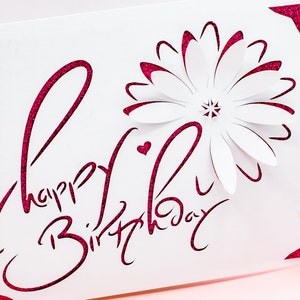 May include: A white card with a pink glitter design that says "Happy Birthday" with a white paper flower in the corner.