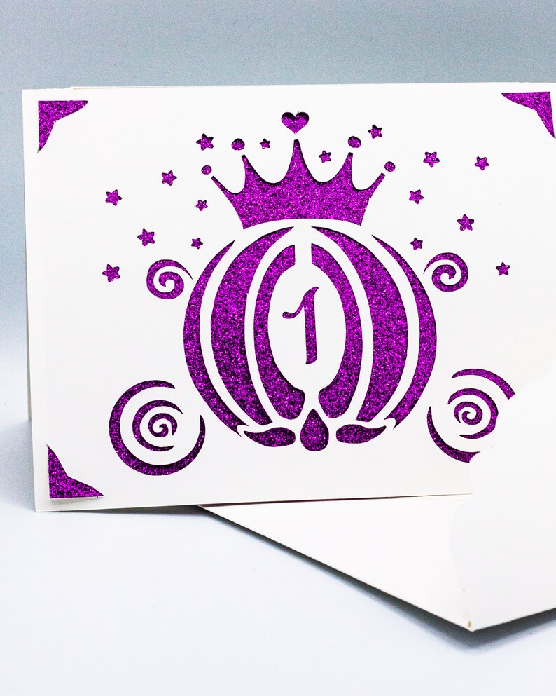 May include: A white card with a purple glitter design of a carriage with a crown on top. The carriage has a number "1" inside. The card is decorated with stars and swirls.