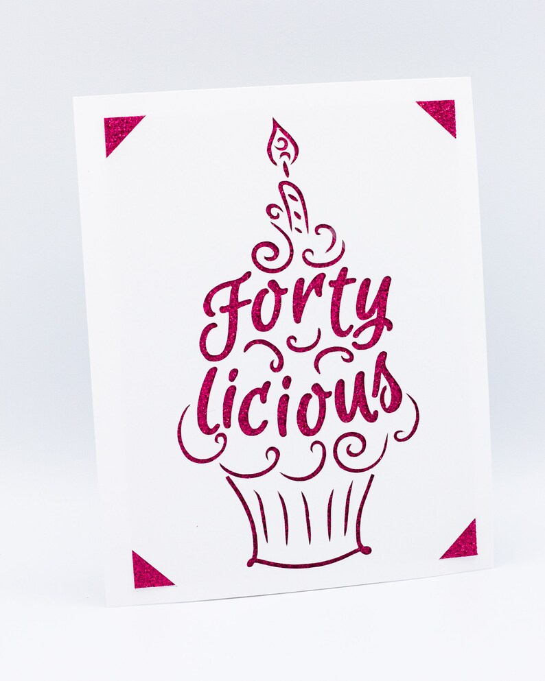 May include: A white card with a pink cupcake design. The cupcake has a candle on top and the words "Forty Licious" written on it.