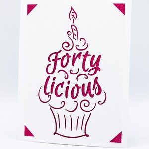 May include: A pink glitter card with a cupcake design and the text "Forty Licious".