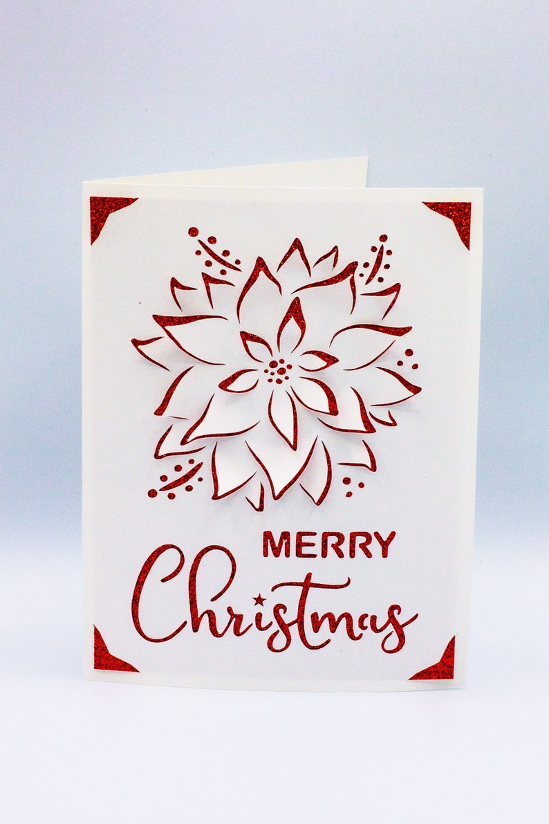 May include: A white card with a red glitter design of a poinsettia flower and the text "Merry Christmas".