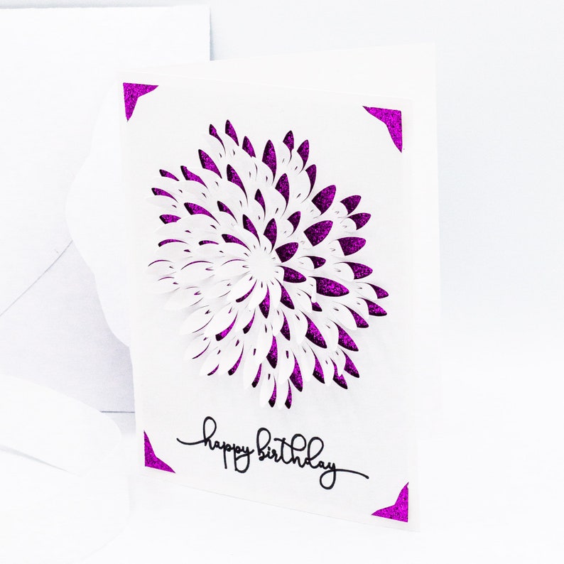 May include: A white card with a purple glitter design of a flower and the text "happy birthday" in black.