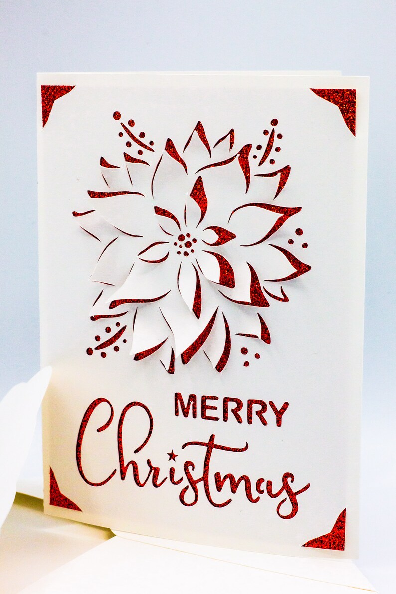 May include: A white card with a red glitter border and a red glitter poinsettia design. The card says "Merry Christmas" in red glitter.