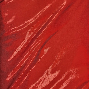 May include: A close-up of a vibrant red fabric with a textured, dotted surface. The material is draped, creating diagonal folds and highlights that catch the light, adding depth and dimension to the textile.