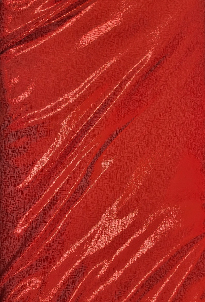 May include: A close-up of a vibrant red fabric with a textured, dotted surface. The material is draped, creating diagonal folds and highlights that catch the light, adding depth and dimension to the textile.