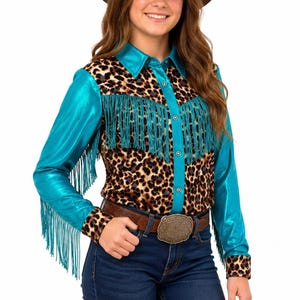 May include: A long-sleeve button-down shirt featuring a leopard print pattern on the torso and cuffs, contrasted with metallic turquoise sleeves, collar, and front placket. The shirt is adorned with long turquoise fringe across the chest and sleeves.