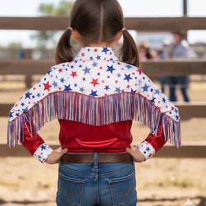 May include: A red, white, and blue star-patterned shirt with fringe. The shirt has a red bodice and long sleeves with star accents. The person is wearing blue jeans and a brown belt. The shirt's design is reminiscent of the American flag.