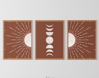 May include: Three framed prints with a minimalist design. The prints feature a sun with rays, a moon in various phases, and another sun with rays. The prints are hung on a white wall above two brown leather armchairs and a coffee table.