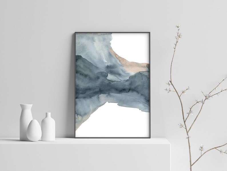 May include: Abstract watercolour painting in shades of blue and grey, framed in a black frame. The painting features a large, abstract shape that resembles a mountain range or a cloud formation.