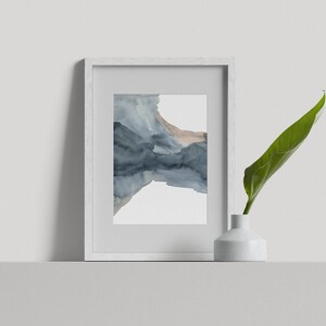 May include: A white frame containing a watercolour painting of abstract blue and brown shapes. The frame is on a white shelf with a white vase and a green leaf.
