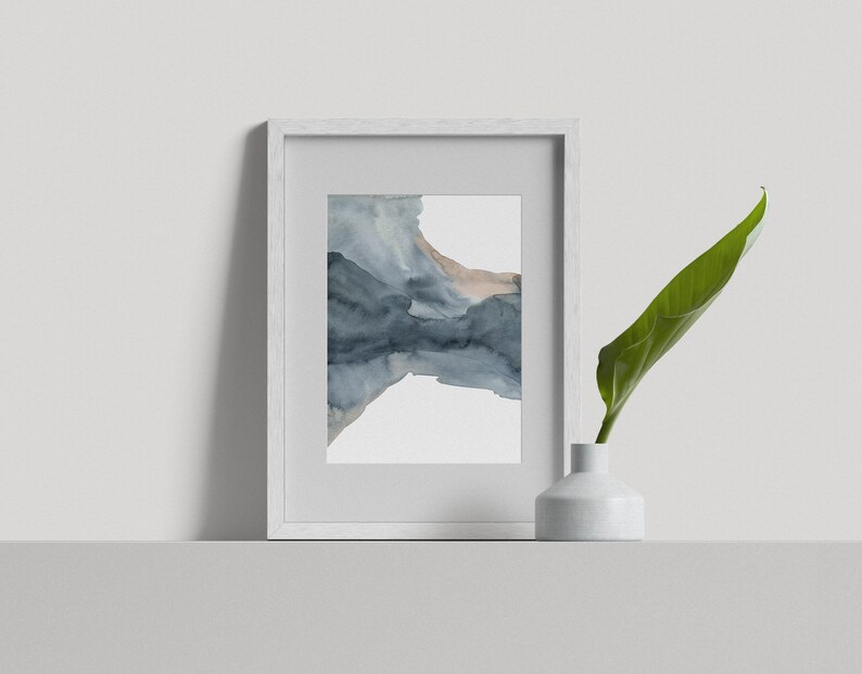May include: A white frame containing a watercolour painting of abstract blue and brown shapes. The frame is on a white shelf with a white vase and a green leaf.
