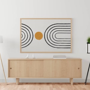 以下が含まれることがあります： 白い背景に黒いアーチ状の線と黄色の円が描かれた、額入りの抽象的なアートプリント。アートワークは、引き戸付きの明るい木製のキャビネットの上に飾られています。フロアランプと黒いスタンドの植物が両側にあります。