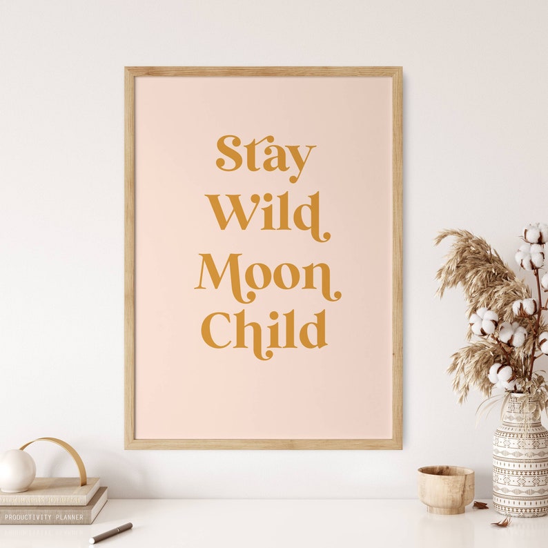 May include: A framed print with a pink background and the text "Stay Wild Moon Child" in a gold color.