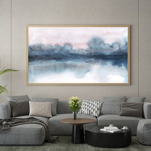 K&ouml;nnte beinhalten: Ein graues Ecksofa mit einer Wolldecke und Kissen in einem Wohnzimmer. Ein abstraktes Aquarellbild in einem Holzrahmen h&auml;ngt an der Wand &uuml;ber dem Sofa. Eine schwarze Stehlampe mit einem Scheinwerfer steht in der Ecke des Raumes.