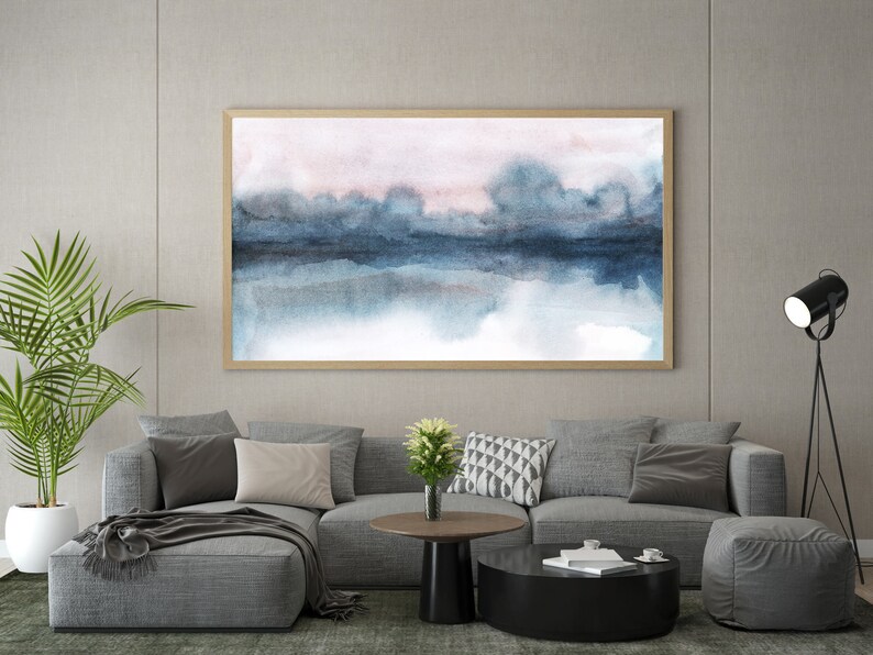 K&ouml;nnte beinhalten: Ein graues Ecksofa mit einer Wolldecke und Kissen in einem Wohnzimmer. Ein abstraktes Aquarellbild in einem Holzrahmen h&auml;ngt an der Wand &uuml;ber dem Sofa. Eine schwarze Stehlampe mit einem Scheinwerfer steht in der Ecke des Raumes.