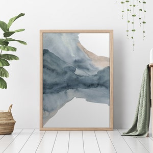 May include: A framed abstract watercolour painting with shades of blue and brown. The painting is on a white background and is hanging on a white wall.