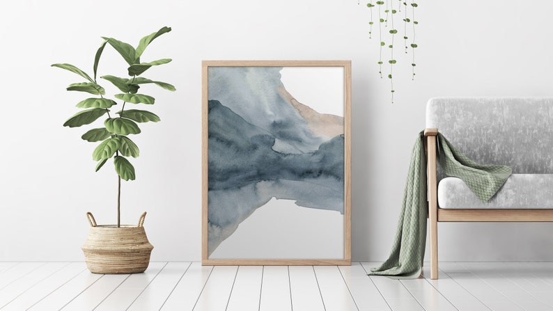 May include: A framed abstract watercolour painting with shades of blue and brown. The painting is on a white background and is hanging on a white wall.