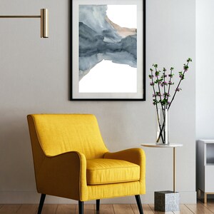May include: A yellow armchair with black legs sits in a room with a framed watercolour painting of a blue and brown abstract design on the wall. A small table with a vase of pink flowers sits next to the chair.