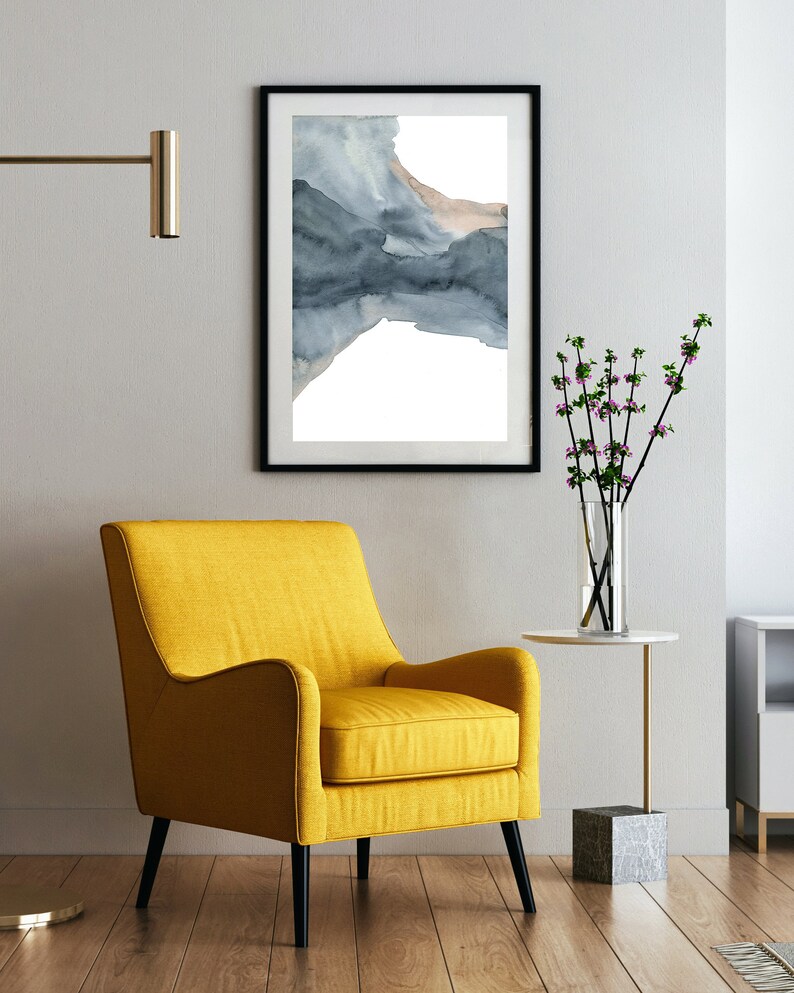May include: A yellow armchair with black legs sits in a room with a framed watercolour painting of a blue and brown abstract design on the wall. A small table with a vase of pink flowers sits next to the chair.