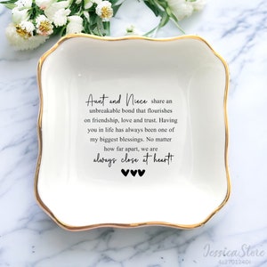 May include: White ceramic trinket dish with a gold rim. The dish has a quote about the unbreakable bond between an aunt and niece. The quote reads: "Aunt and Niece share an unbreakable bond that flourishes on friendship, love and trust. Having you in life has always been one of my biggest blessings. No matter how far apart, we are always close at heart!"