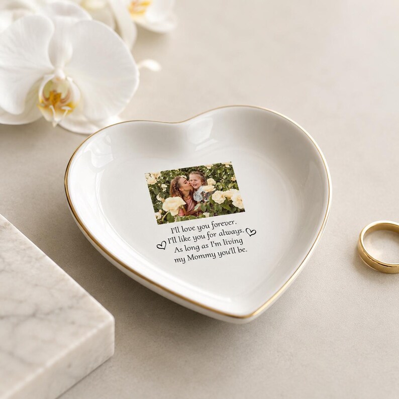 May include: A white heart-shaped ceramic trinket dish with a gold-toned rim. The center features a printed photograph of two people among yellow flowers, with the text: I'll love you forever. I'll like you for always. As long as I'm living my Mommy you'll be.
