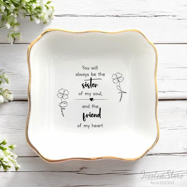 May include: A square white ceramic trinket dish with a gold-painted scalloped rim. The center features black text reading: You will always be the sister of my soul, and the friend of my heart, flanked by two clover illustrations with names.