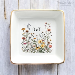May include: Square white ceramic trinket dish with a gold rim. The dish features a floral design with colourful wildflowers and the letters "D♥T" in black. A decorative piece for a desk or dresser.
