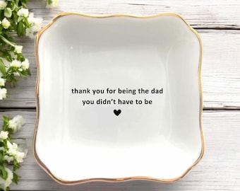 Könnte beinhalten: Weißes Keramik-Schmuckschälchen mit goldenem Rand und dem Text "thank you for being the dad you didn't have to be" mit einem schwarzen Herz. Die Schale hat eine quadratische Form mit abgerundeten Kanten.