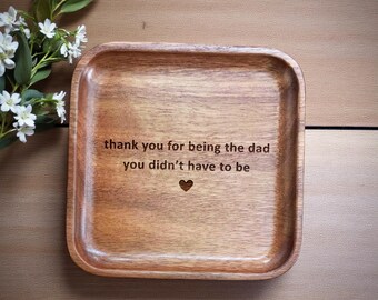 Könnte beinhalten: Ein quadratisches Holztablett mit abgerundeten Kanten, graviert mit dem Text "thank you for being the dad you didn't have to be" und einem Herzsymbol. Das Tablett hat eine warme braune Farbe und liegt auf einer Holzoberfläche.