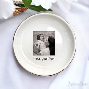 Puede incluir: Plato de cer&aacute;mica blanca para alhajas con borde dorado. El plato presenta una foto en blanco y negro de una madre y un hijo con el texto "I love you Mom".
