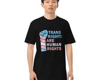 May include: Black t-shirt featuring a raised fist graphic in the colours of the transgender pride flag. The text "Trans Rights Are Human Rights" is printed on the shirt.