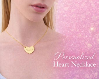 May include: A gold-colored heart-shaped pendant necklace with the name "Hannah" engraved on it. The necklace is on a delicate chain. The background is a soft pink with the text "Personalized Heart Necklace".