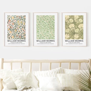 May include: Three framed prints of William Morris floral patterns. The prints are in a light wood frame and feature a green and white floral pattern, a green and white leaf pattern, and a yellow and green floral pattern. The prints are hung on a white wall.