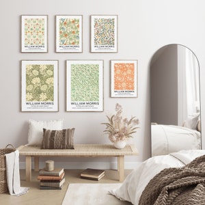 May include: A set of six framed prints featuring floral patterns by William Morris. The prints are in a variety of colors, including green, orange, and yellow. The prints are hung on a white wall above a wooden bench.