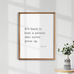 May include: A framed print with a white background and black text that reads "It's hard to beat a person who never gives up. - Babe Ruth".